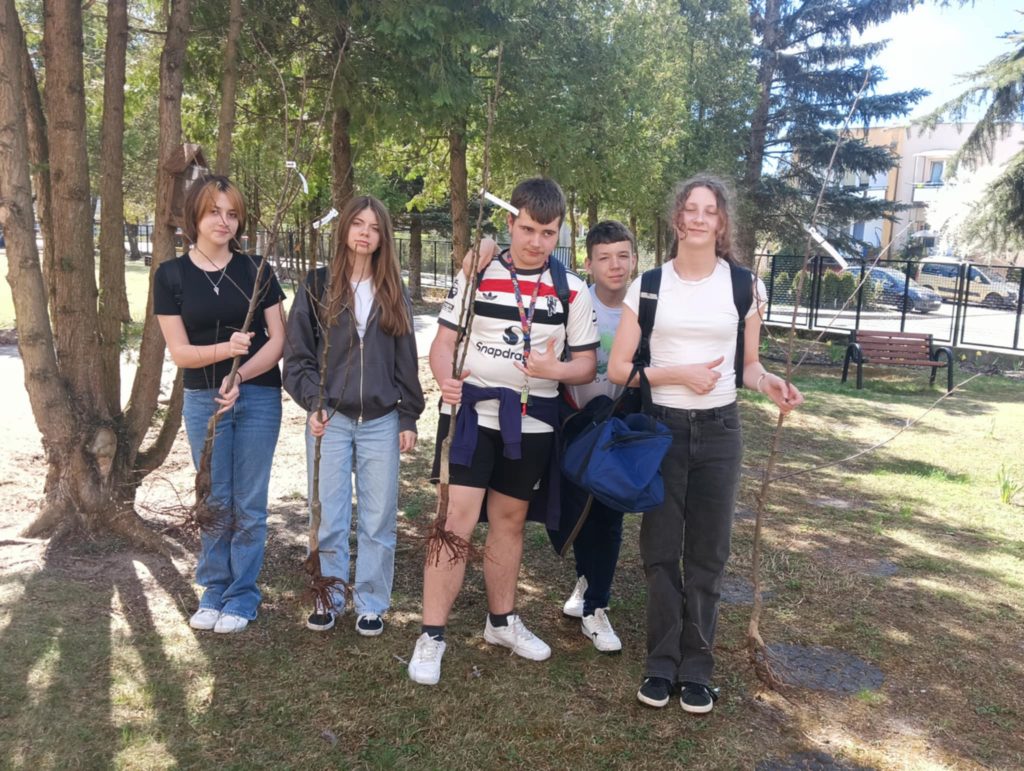 Uczniowie z drzewkami w szkolnym ogrodzie